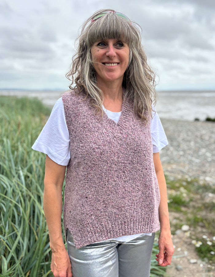 Woman wearing a pink knitted vest standing outdoors with a natural background