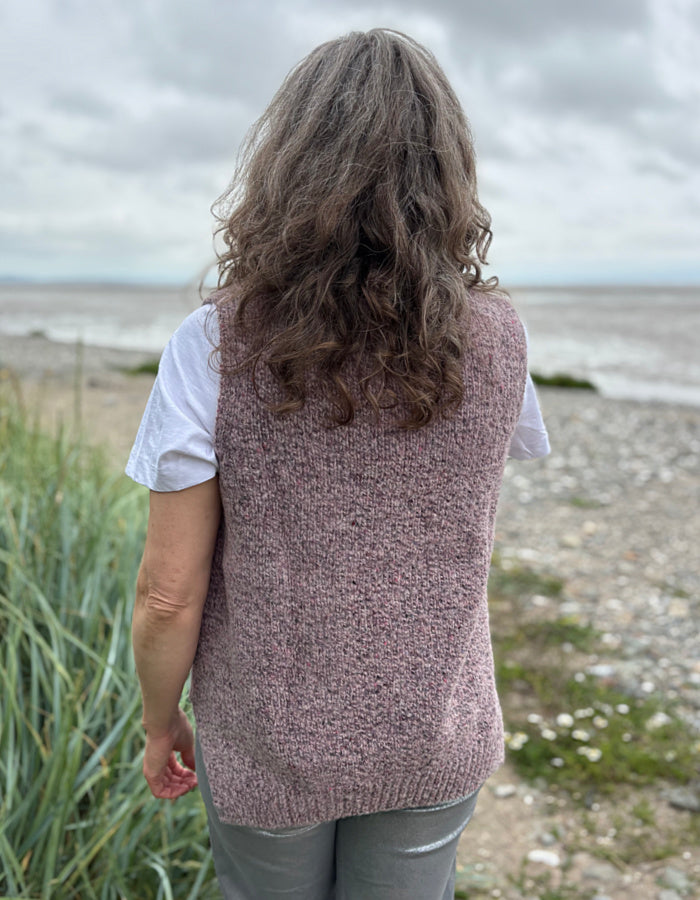 Person wearing a pink knitted vest standing on a beach