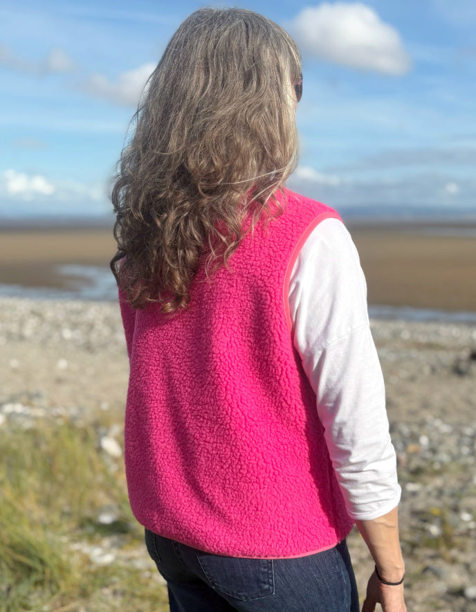 Person wearing a pink fleece vest on a beach with a blue sky and clouds in the background