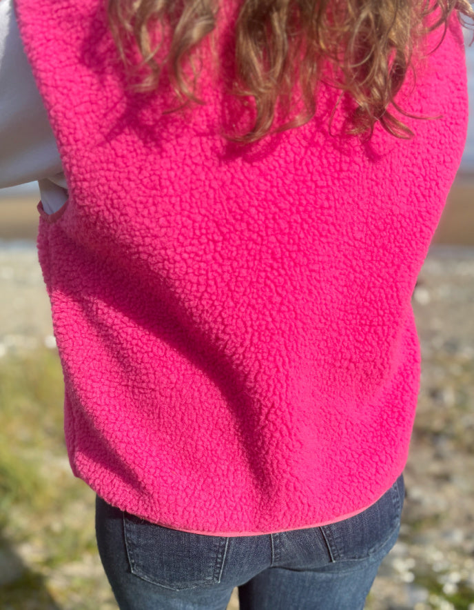 Person wearing a bright pink fleece vest with a blurred natural background