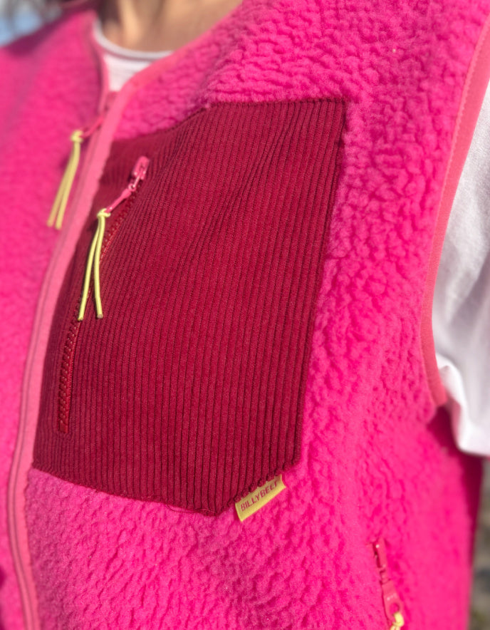 Close-up of a pink fleece jacket with a red pocket and yellow zipper.