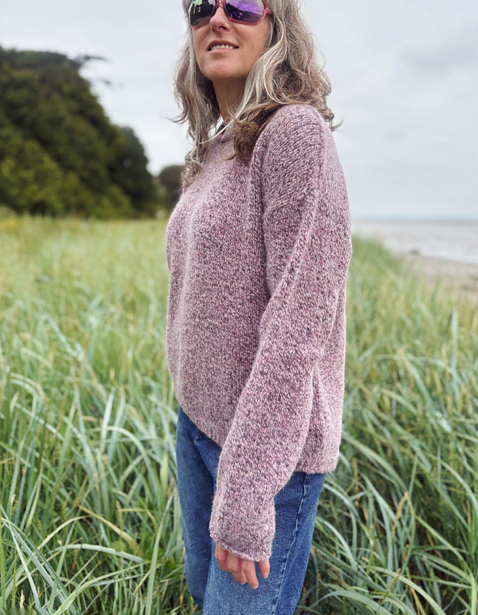 Person wearing a donegal tweed pink sweater and sunglasses in a grassy outdoor setting