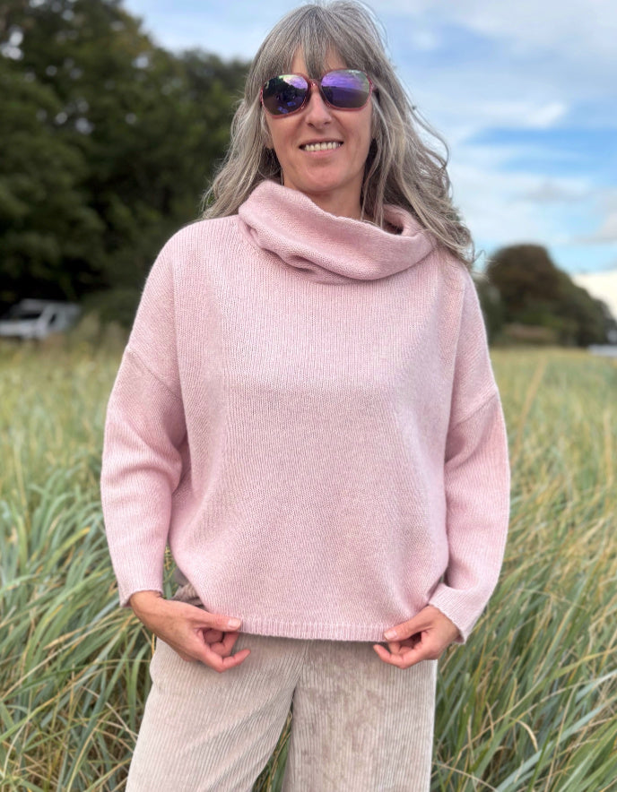 Woman wearing a pink sweater and sunglasses in a grassy field