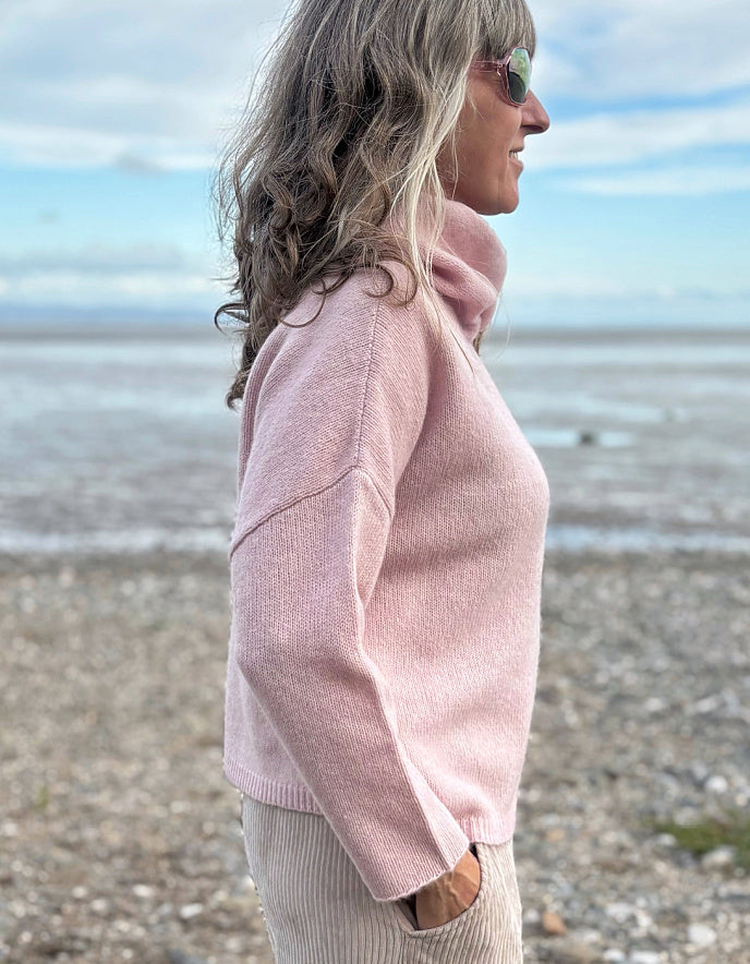 Woman wearing a pink sweater on a beach with a blue sky and ocean in the background