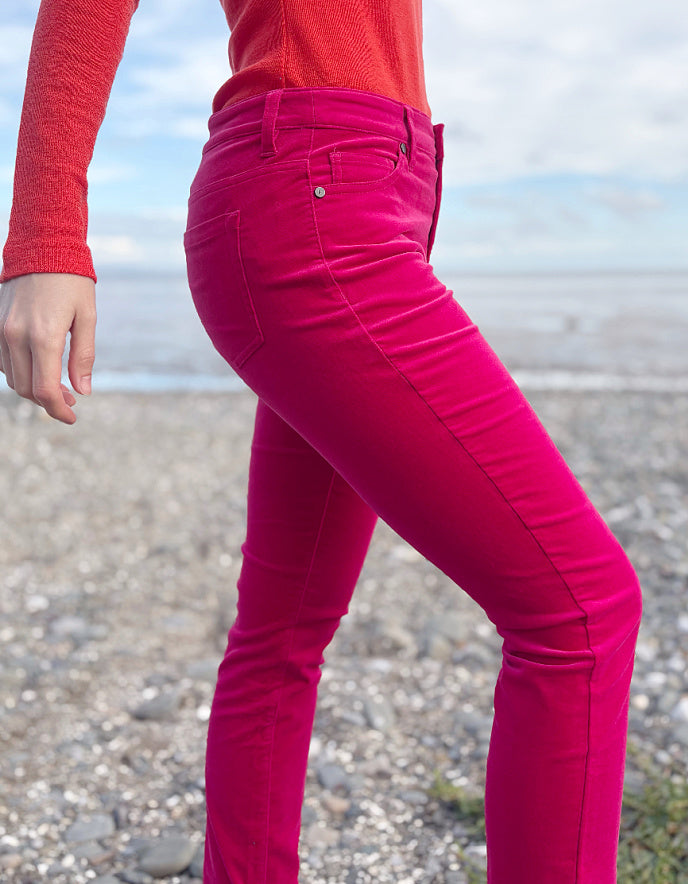 Person wearing a red sweater and pink velvet jeans standing on a beach.
