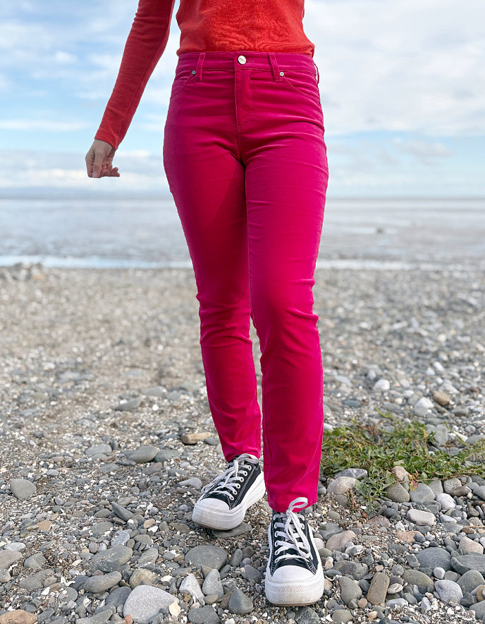 Person wearing a red sweater and pink velvet jeans standing on a beach.