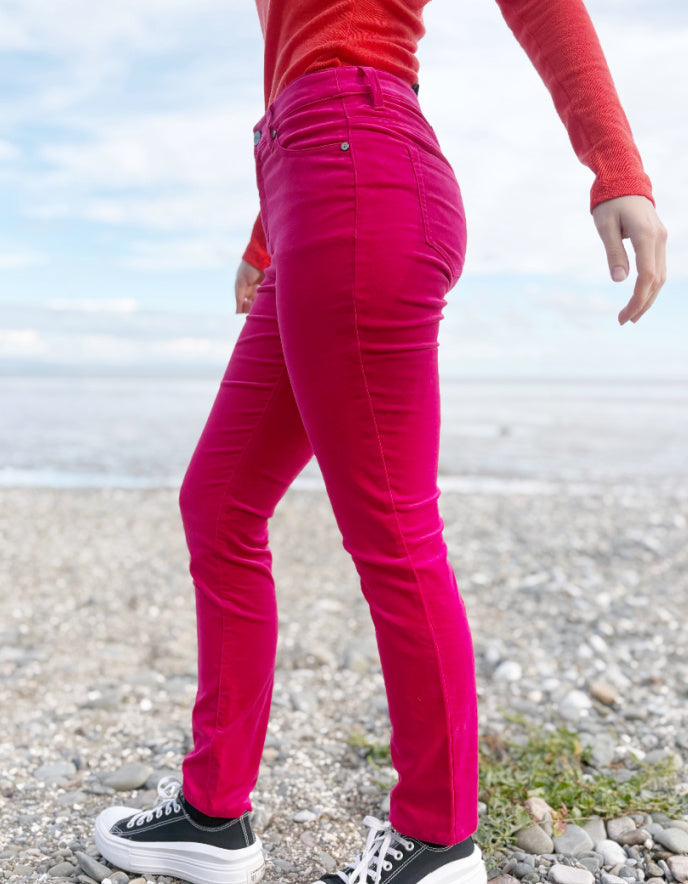 Person wearing a red sweater and pink velvet jeans standing on a beach.