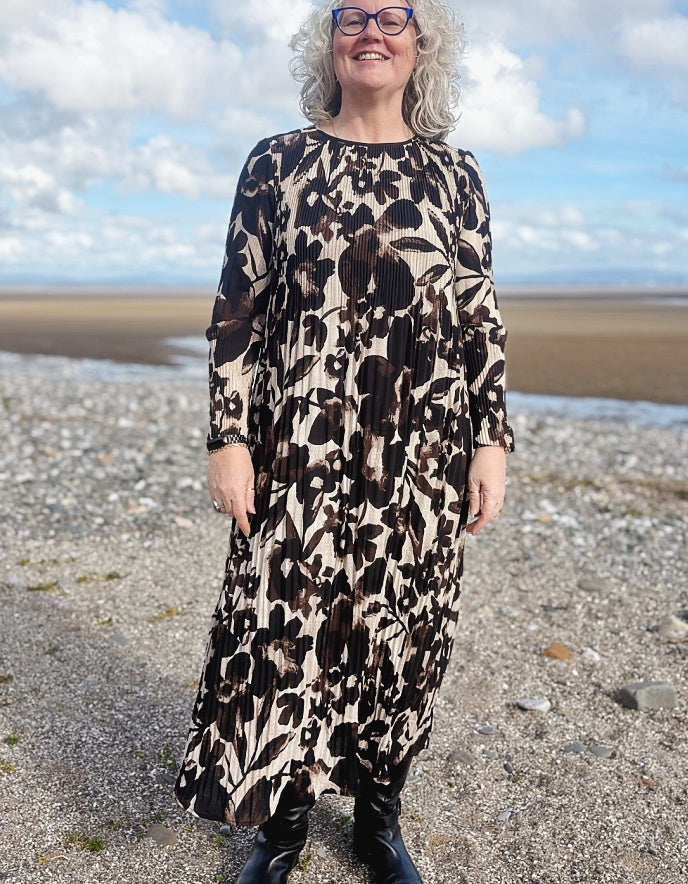 Woman wearing a patterned dress standing on a beach with a blue sky and clouds in the background.