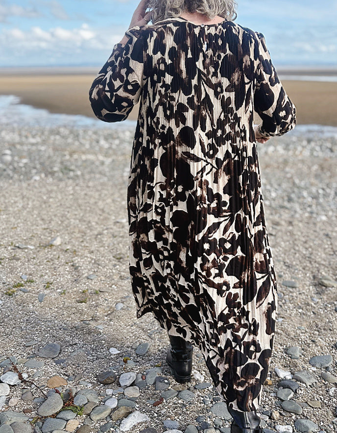 Person wearing a leopard print dress standing on a pebbly beach.