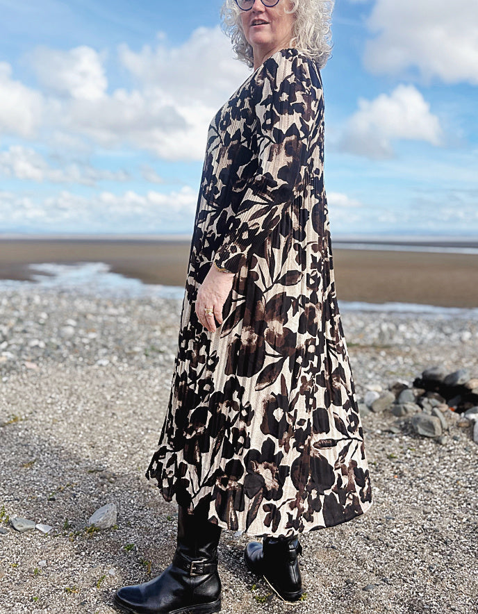 Woman in a patterned dress standing on a beach with a blue sky and ocean in the background