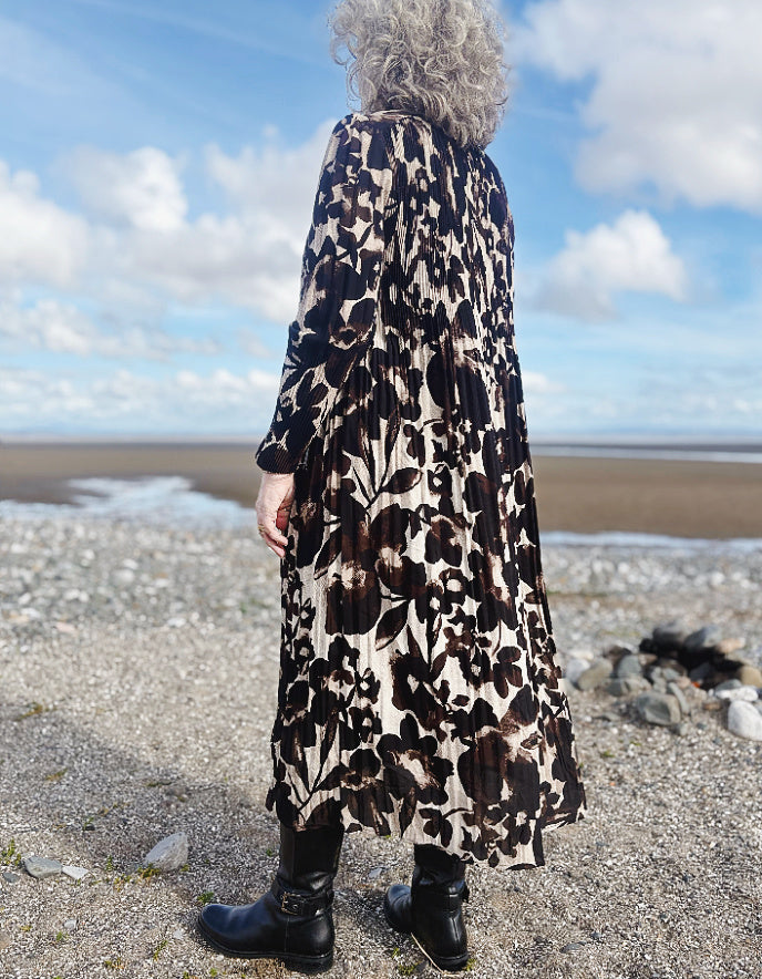 Person wearing a long, patterned coat standing on a beach with a blue sky and clouds in the background.