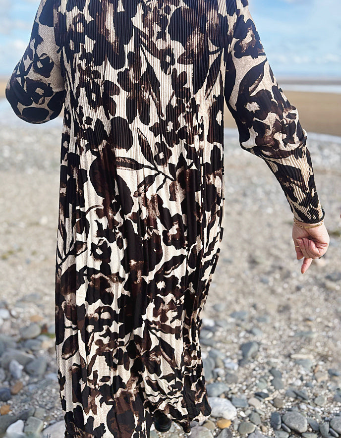 Person wearing a long, patterned dress on a pebbly beach.