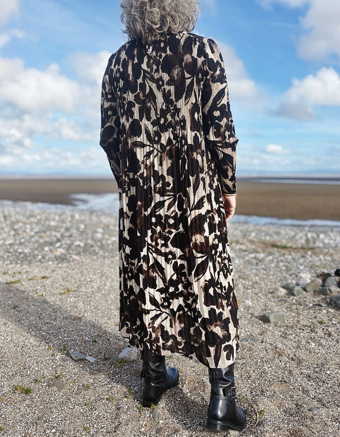 Person wearing a long leopard print coat standing on a beach with a blue sky.