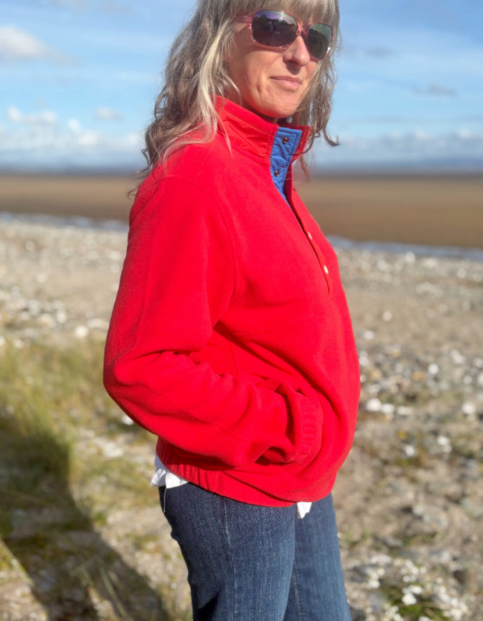 Person wearing a red jacket with a blue lining on a beach