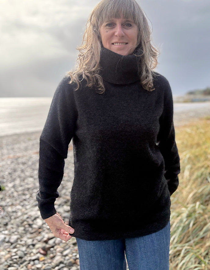 Woman wearing a black turtleneck sweater standing on a beach.