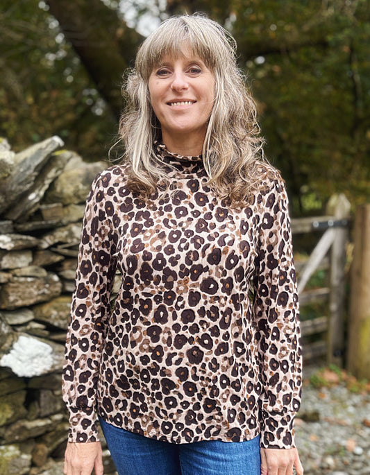 Woman wearing a leopard print long-sleeve top standing in front of a stone wall and trees.