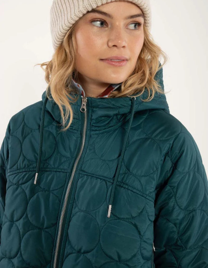 Person wearing a teal quilted jacket and beige beanie on a white background