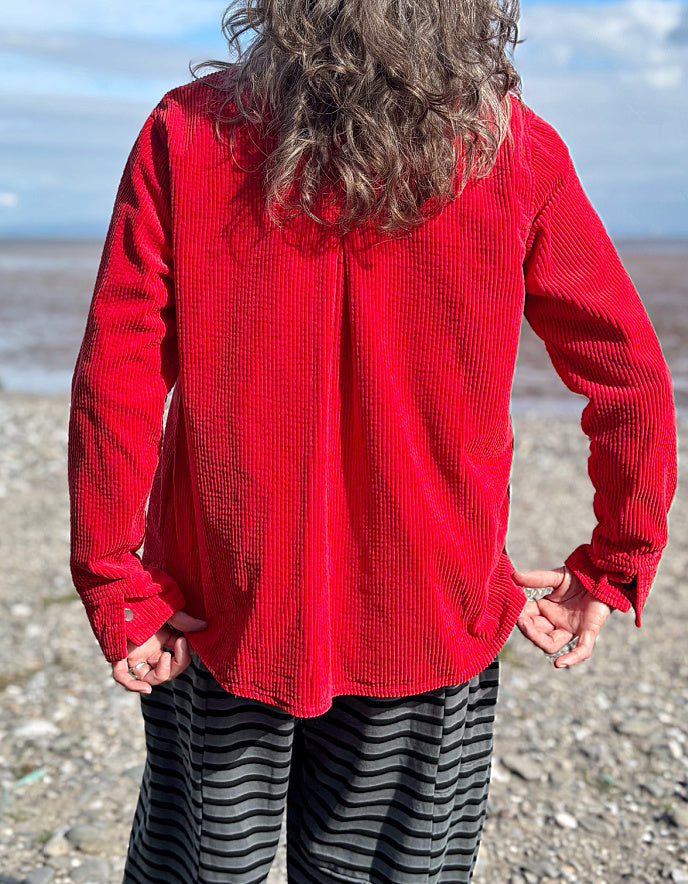 Person wearing a red jacket cord shirt over a red and black striped shirt on a beach