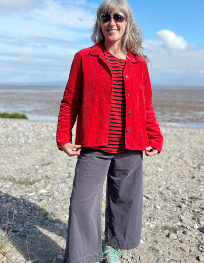 Person wearing a red jacket cord shirt over a red and black striped shirt on a beach