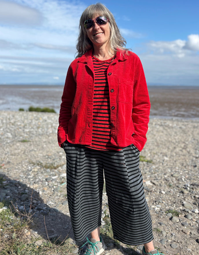 Person wearing a red jacket cord shirt over a red and black striped shirt on a beach