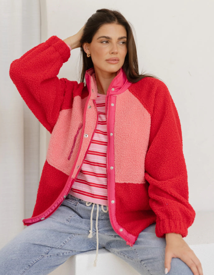 Woman wearing a red and pink jacket with a striped shirt and jeans on a white background