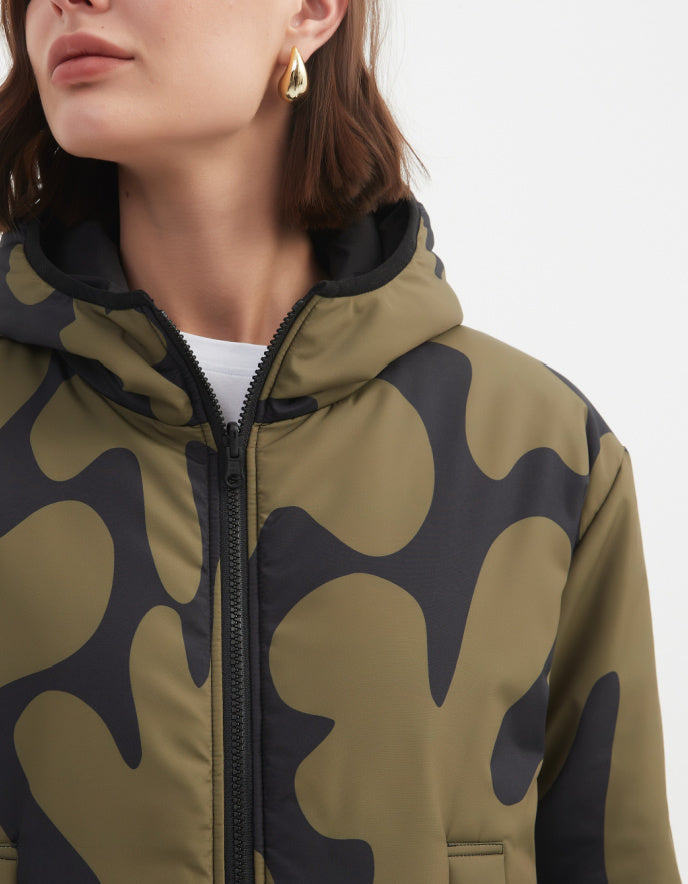 Woman wearing a camouflage olive and black reversible puffer jacket on a white background