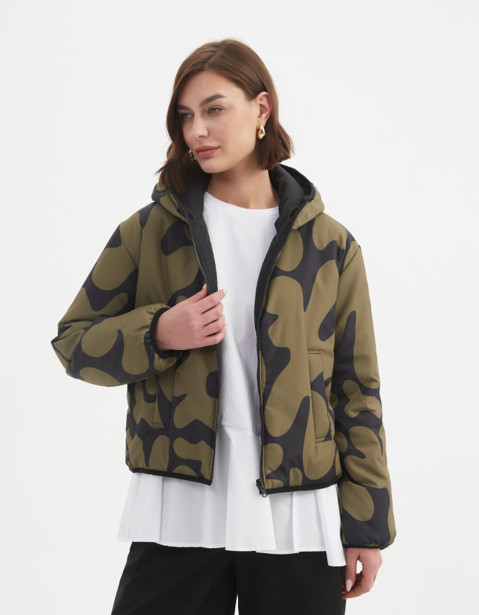 Woman wearing a camouflage olive and black reversible puffer jacket on a white background