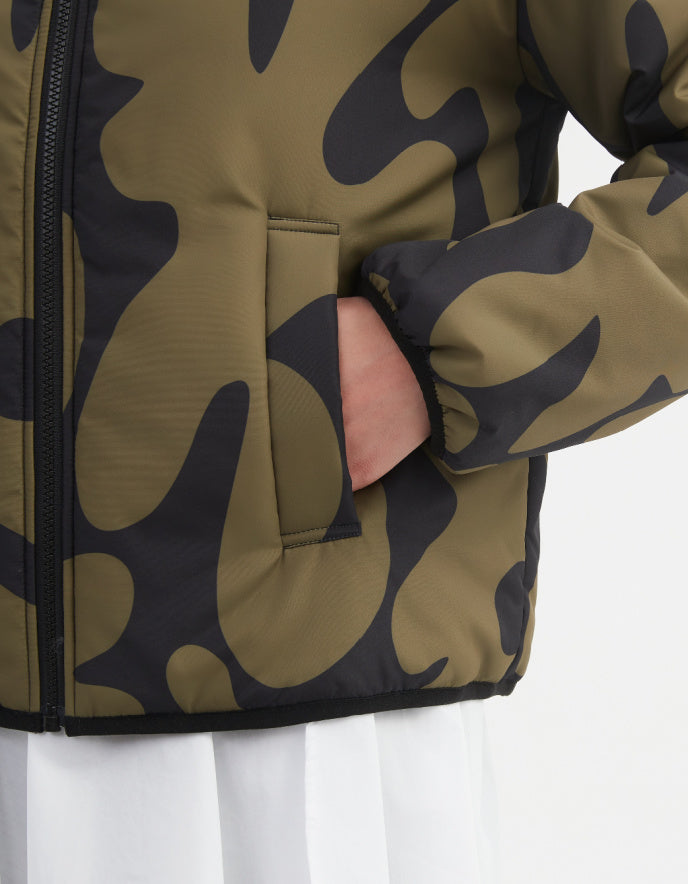 Woman wearing a camouflage olive and black reversible puffer jacket on a white background