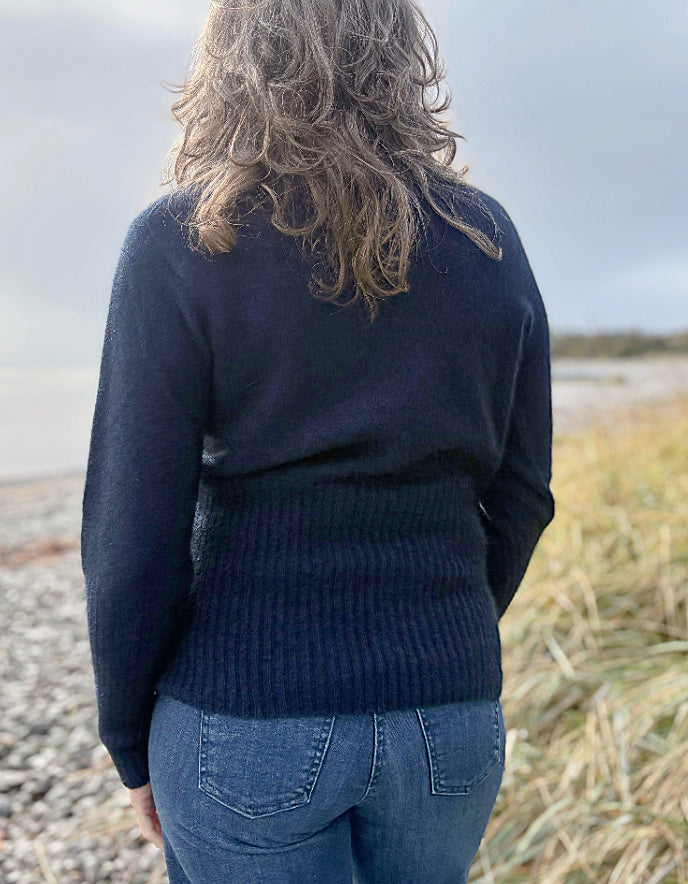 Person wearing a dark blue sweater and jeans standing on a beach.