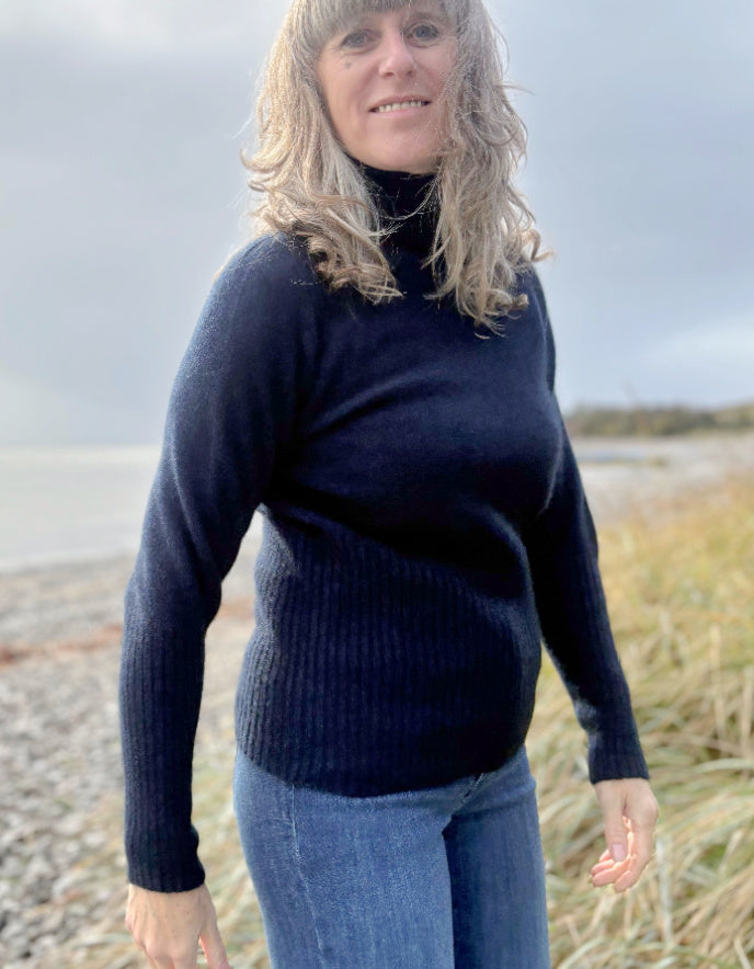 Woman wearing a navy sweater and blue jeans standing on a beach.