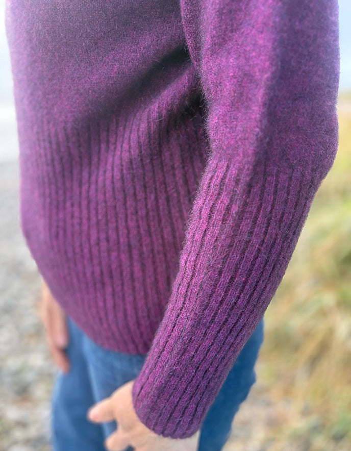 Close-up of a person wearing a purple sweater with a blurred natural background