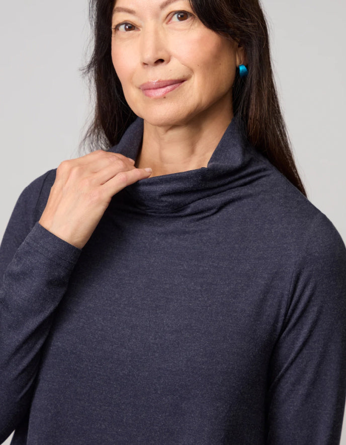Woman wearing a dark blue long-sleeve top with a cowl neck against a gray background