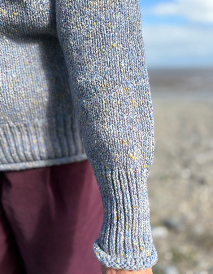Close-up of a person wearing a textured gray sweater with a blurred natural background