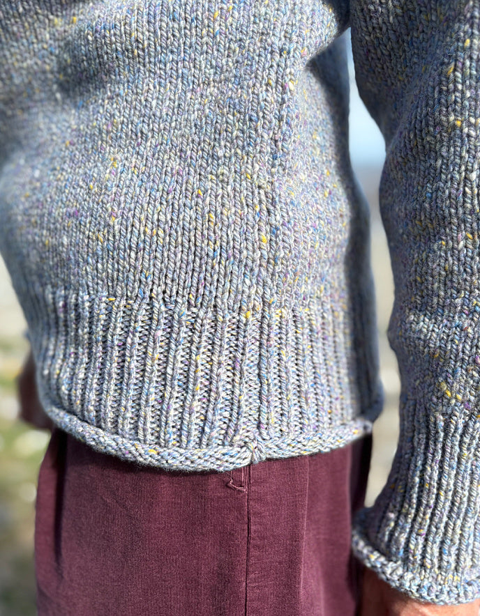 Close-up of a person wearing a textured gray sweater with a blurred natural background