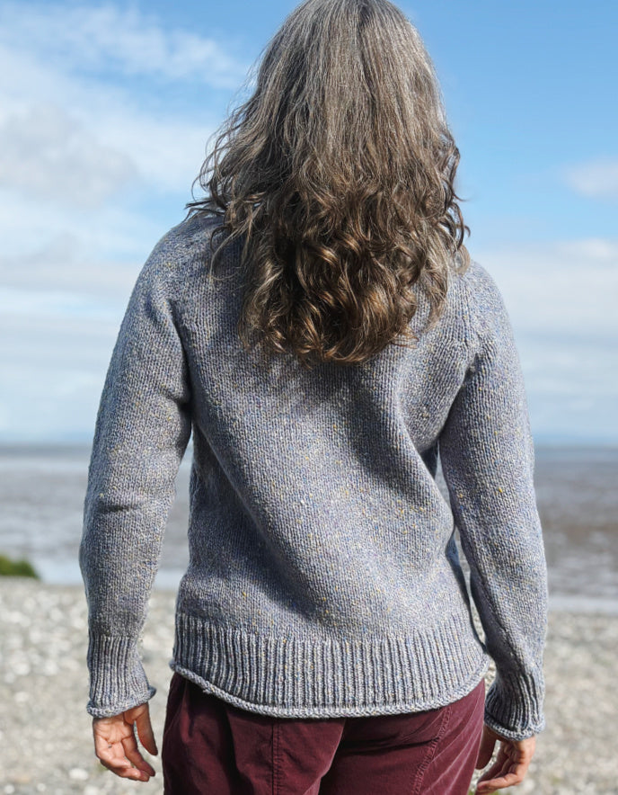 Person wearing a gray sweater standing on a beach with a cloudy sky.