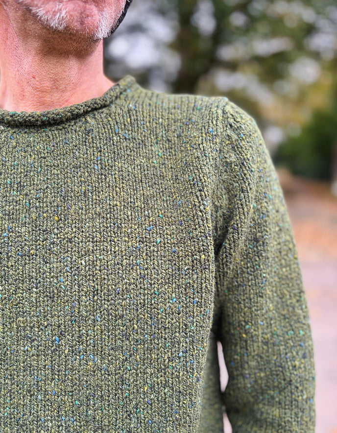 Person wearing a green knitted sweater with a blurred natural background