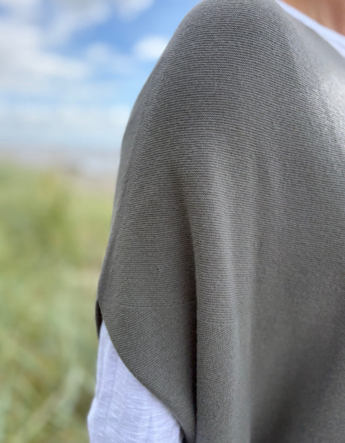 Woman wearing green slate grey tank top with relaxed fit over a white t shirt on a beach and blue sky in the background