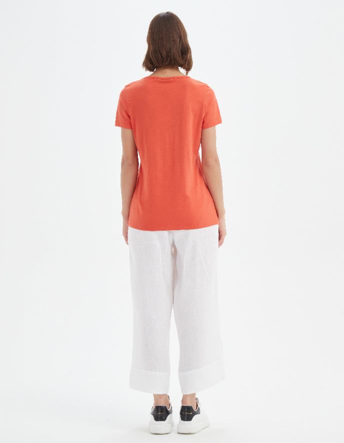 Person wearing an orange t-shirt and white pants on a white background