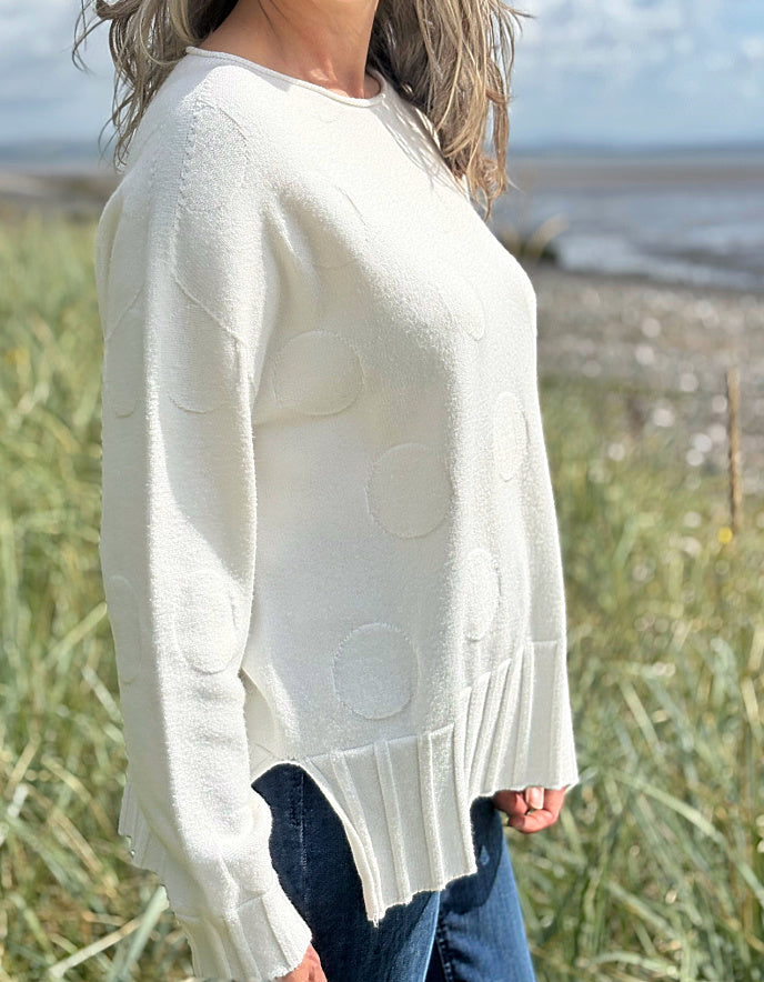 Person wearing a white sweater with circular patterns in an outdoor setting.