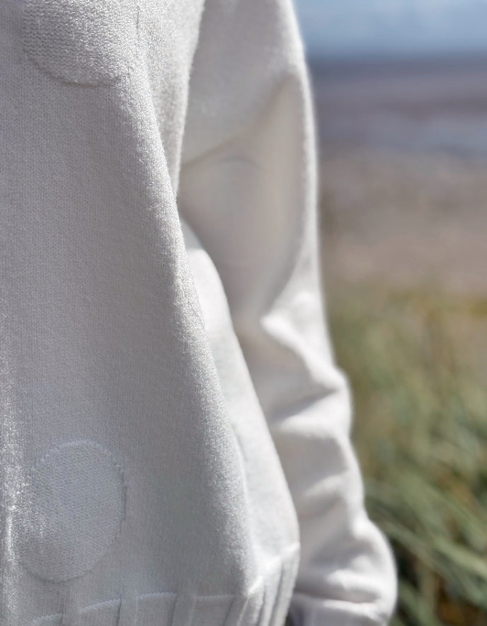 Close-up of a light gray sweater with a blurred natural background