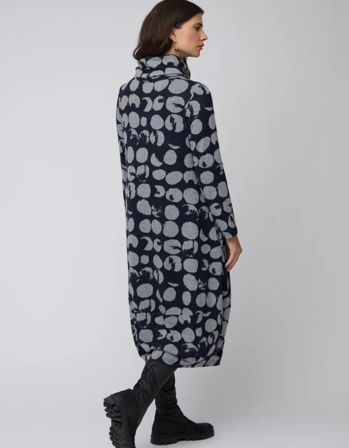 Woman wearing a long, dark blue coat with light gray abstract patterns on a white background