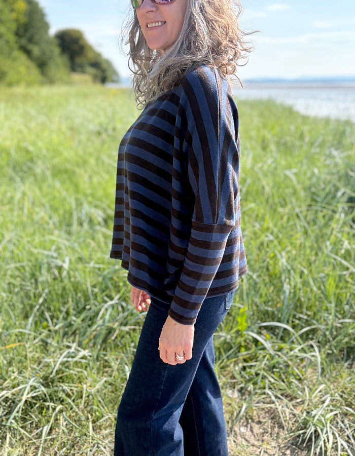 Woman wearing a striped sweater and sunglasses standing in a grassy field with a body of water in the background.