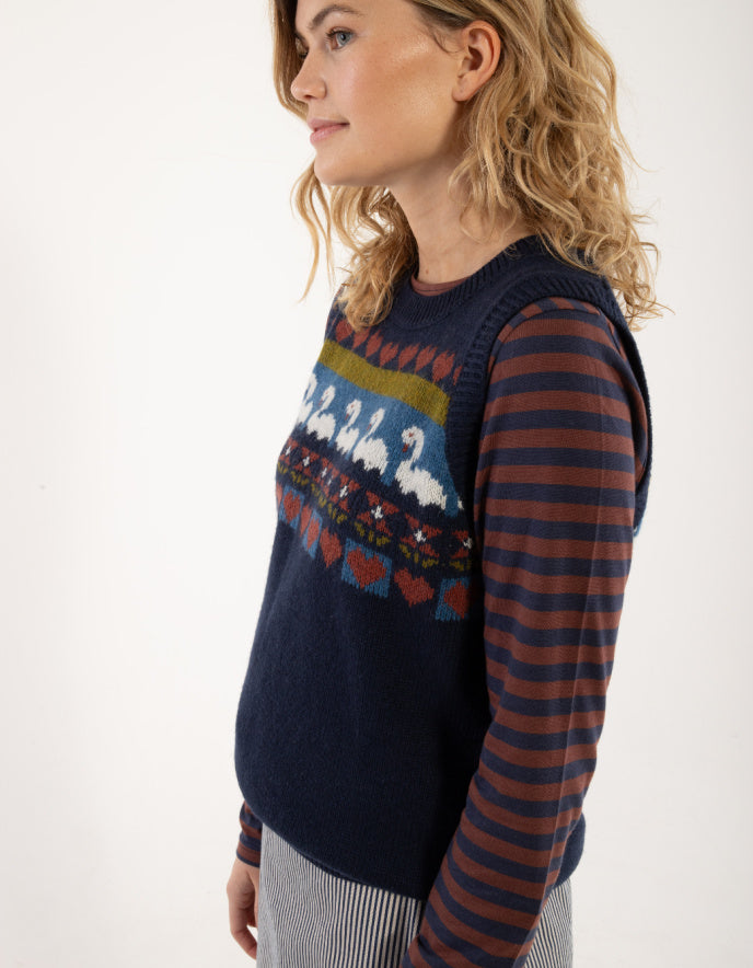 Woman wearing a navy sweater with a colorful pattern and a striped shirt underneath on a white background