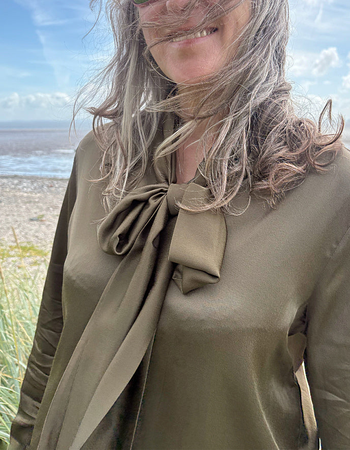 Person wearing a green blouse with a large bow tie, standing on a beach.