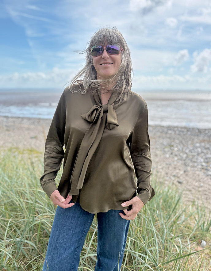 Person wearing a olive silky blouse with a bow tie in a field