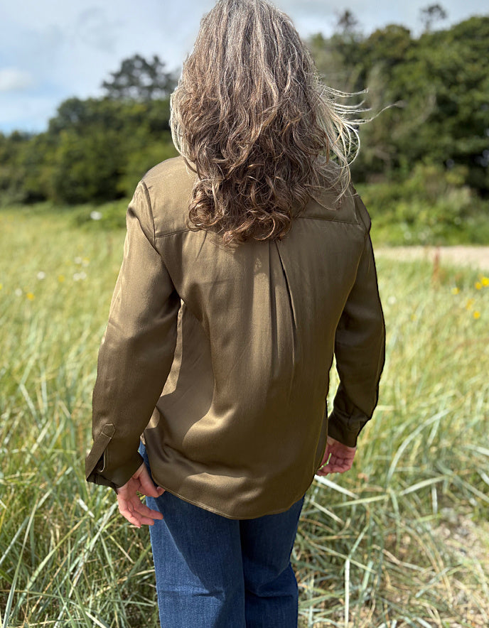 Person wearing a olive silky blouse with a bow tie in a field