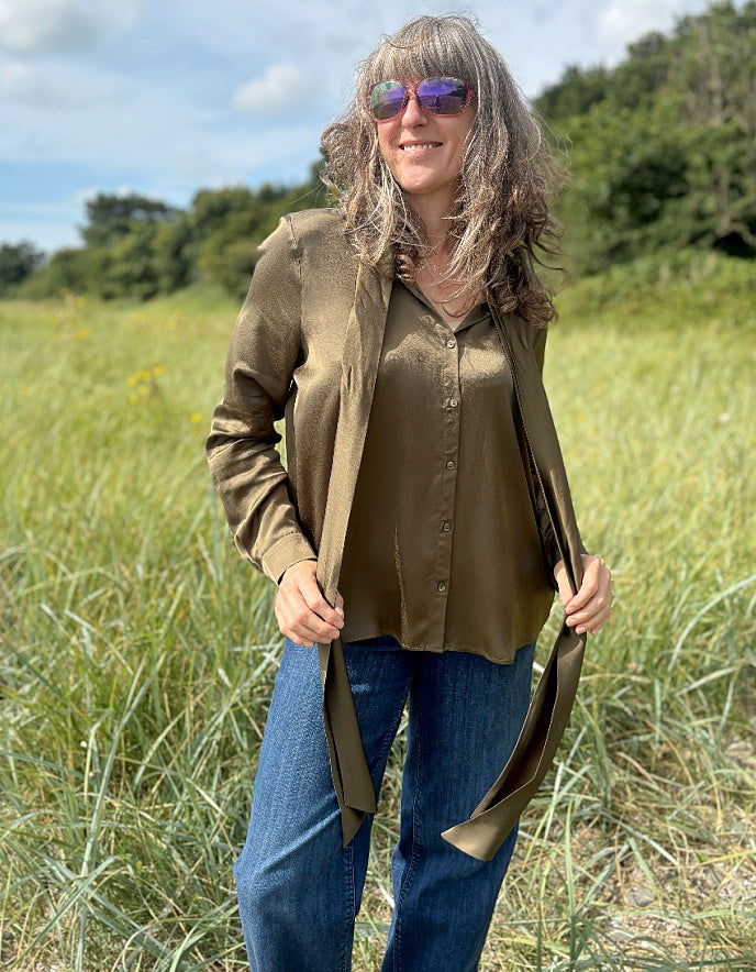Person wearing a olive silky blouse with a bow tie in a field