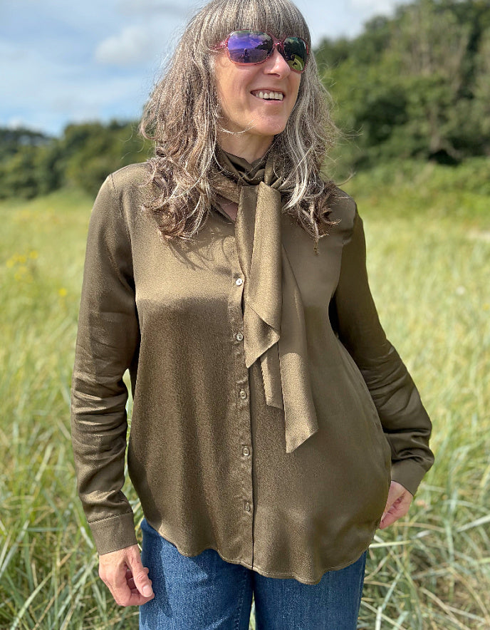 Person wearing a olive silky blouse with a bow tie in a field