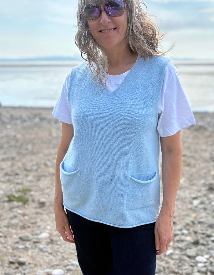 Woman wearing a light blue vest over a white shirt on a beach.