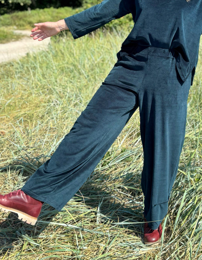 Person wearing teal velvet pants and red shoes standing in a grassy field.